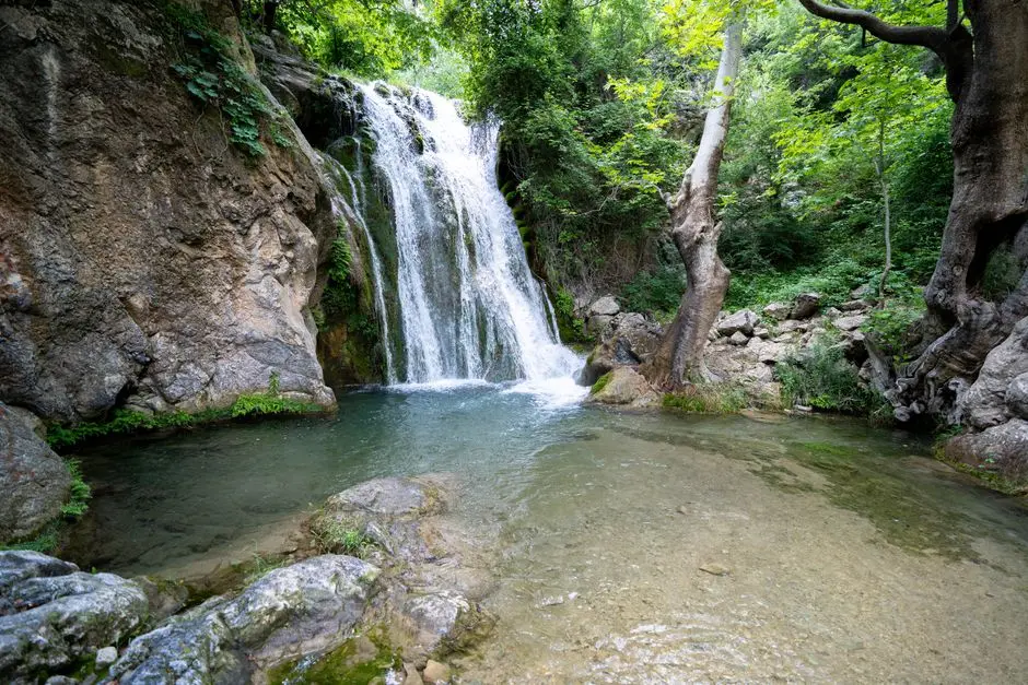 Air terjun alami dengan kolam biru kehijauan dikelilingi pepohonan hijau
